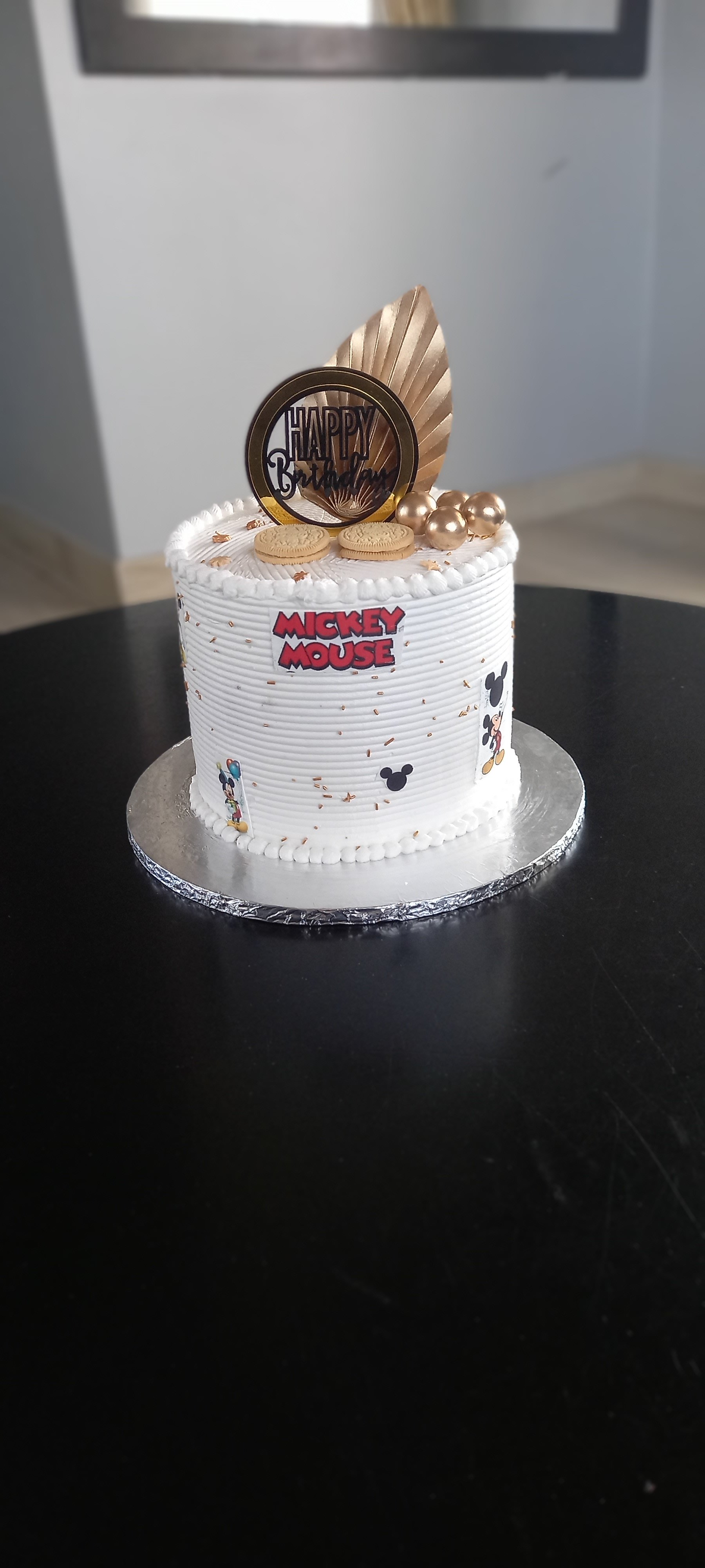 White Mickey Mouse birthday cake with gold accents and feather topper